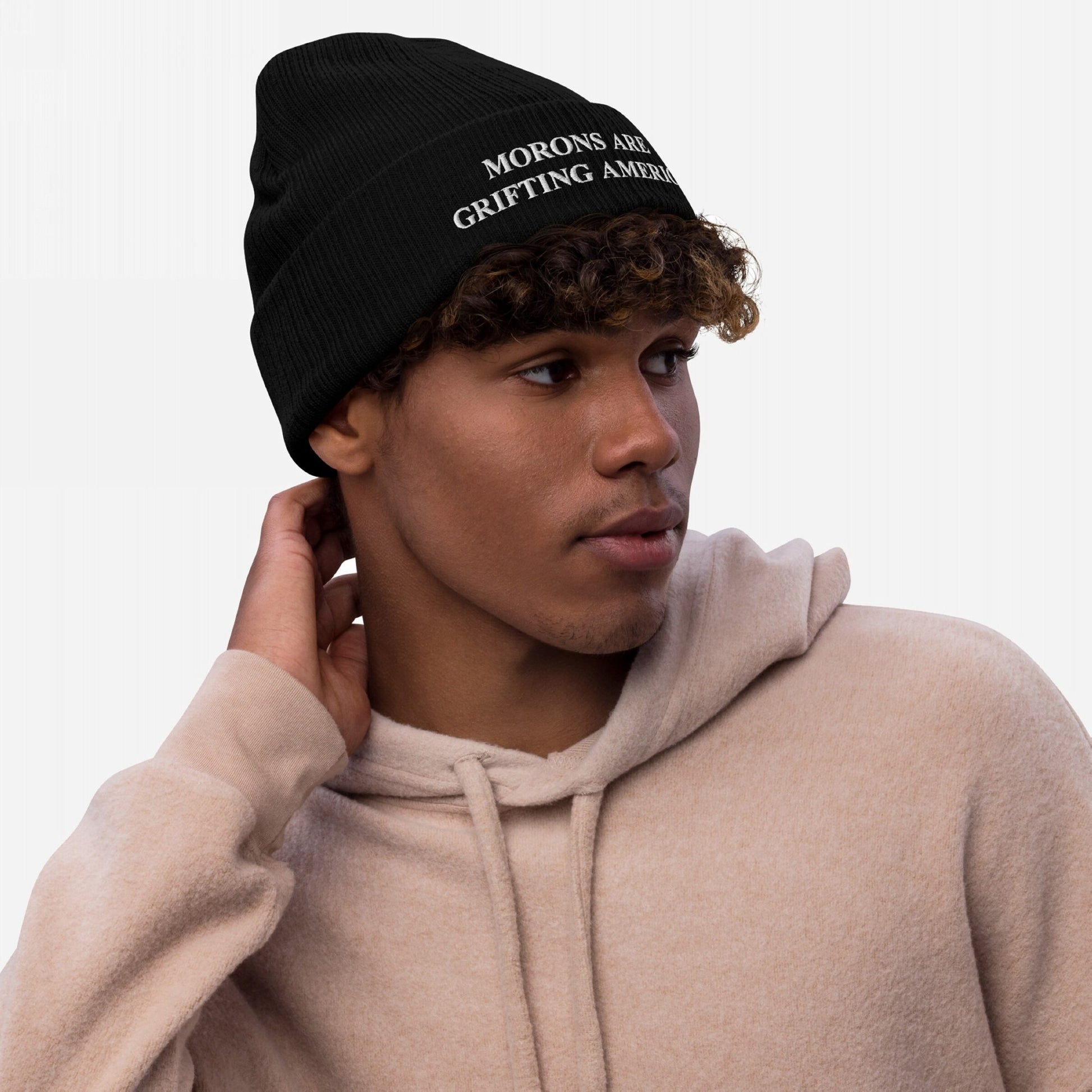 A lifestyle image of a person wearing the black anti-MAGA beanie embroidered with "MORONS ARE GRIFTING AMERICA," styled casually with a light beige hoodie, showcasing the hat’s fit and bold message in everyday wear.