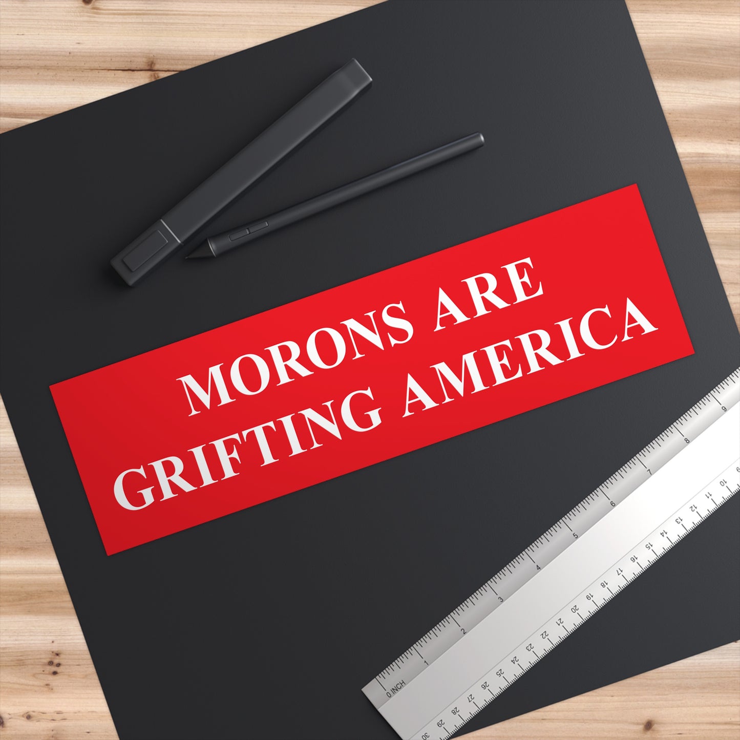 Close-up of red Morons Are Grifting America sticker on a black surface