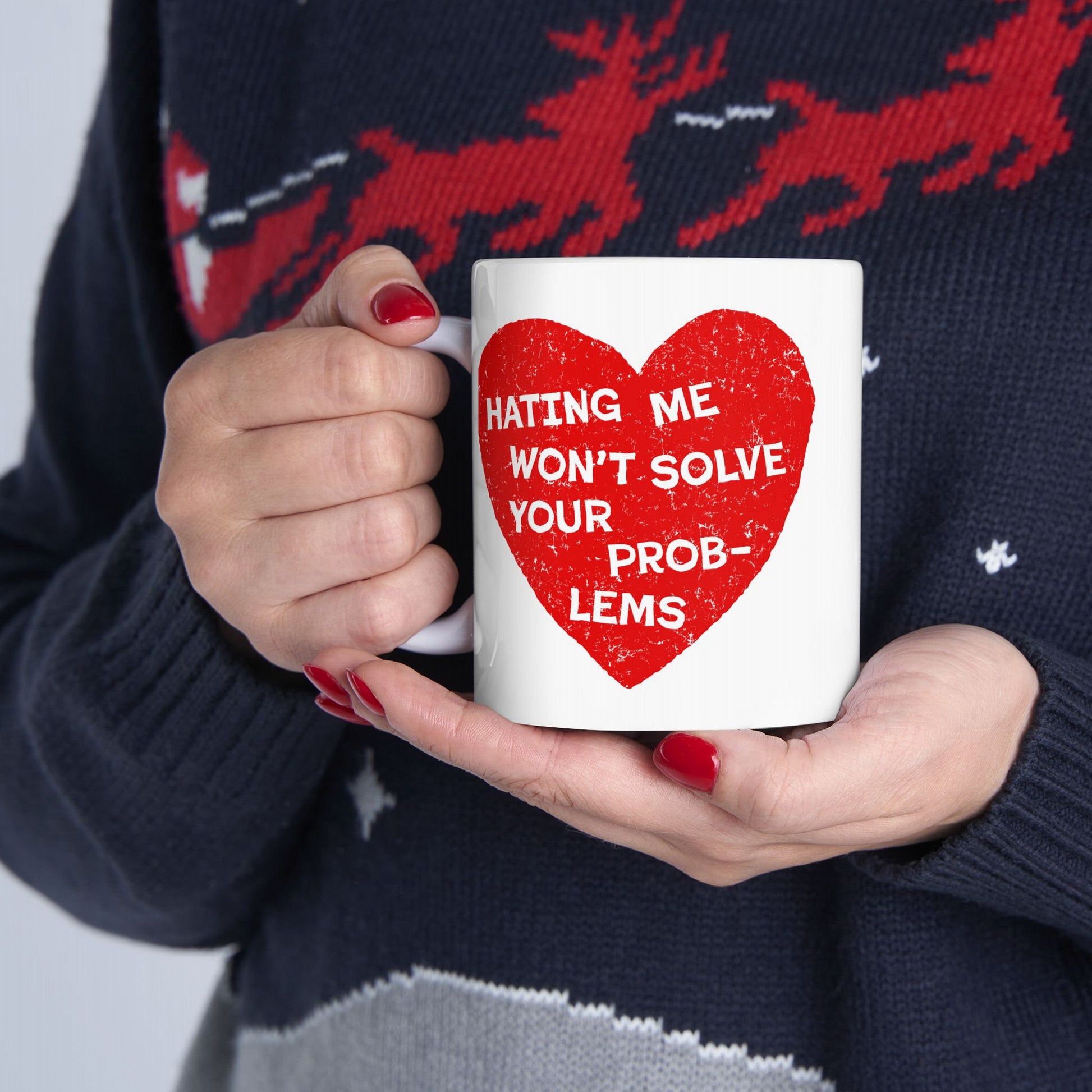 Person in a holiday sweater holds the No Hate Mug, featuring a red heart with the phrase HATING ME WON’T SOLVE YOUR PROBLEMS, embodying empowerment and activism.