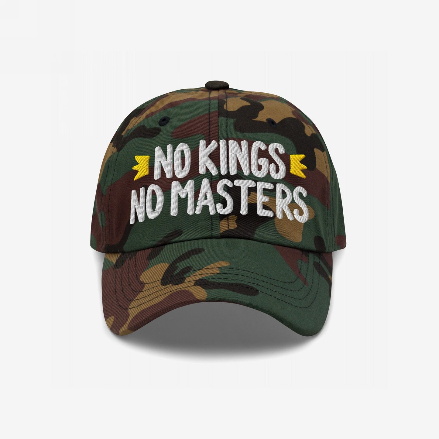 Camouflage-pattern baseball cap with NO KINGS NO MASTERS slogan and yellow crowns, embodying rebellion and anti-authoritarian spirit, reflecting the ethos of equality and defiance.