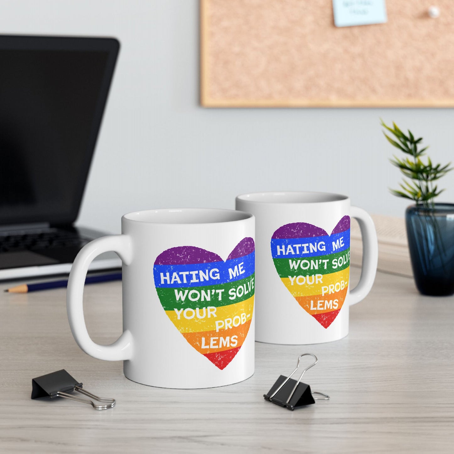 No LGBTQ Hate Mug featuring a distressed rainbow-striped heart and slogan, “Hating me won’t solve your problems,” on a light-wood desk, symbolizing pride and defiance.