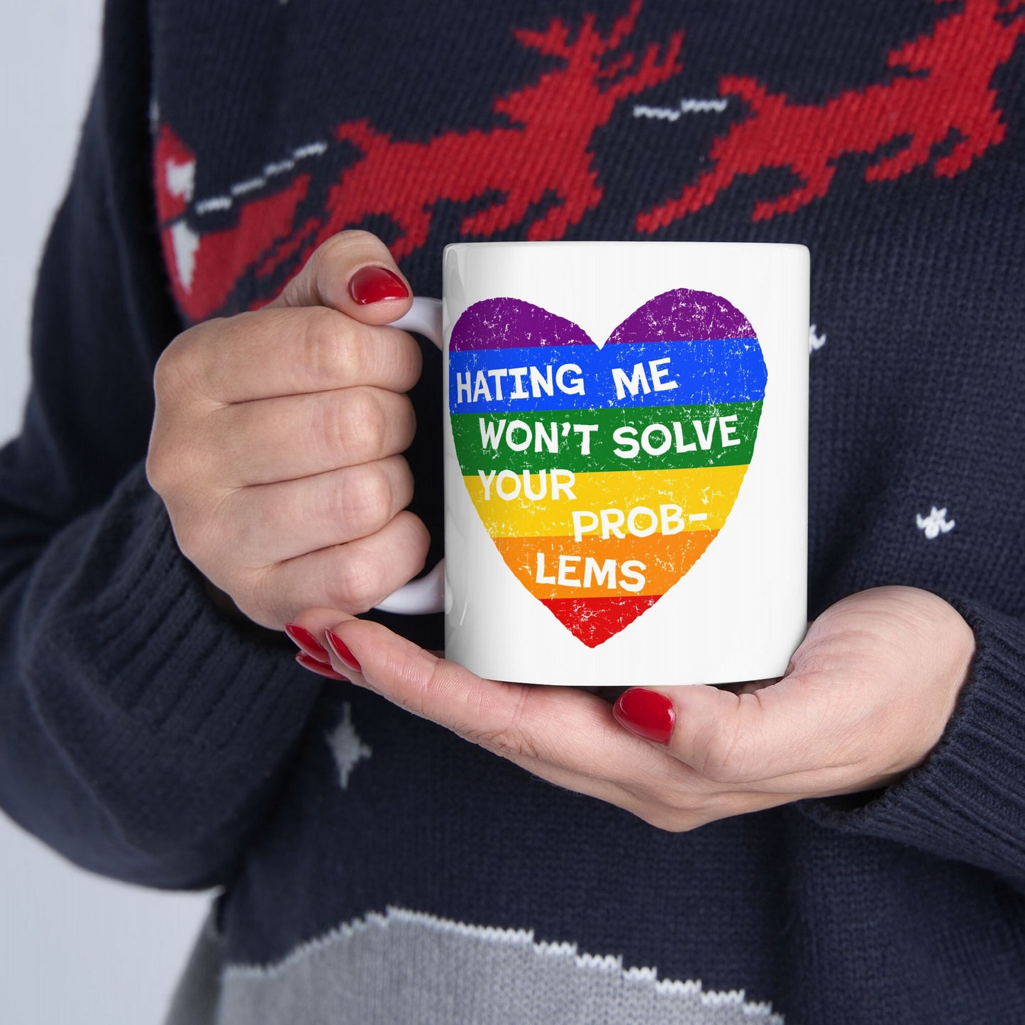 Person holding No LGBTQ Hate Mug with rainbow heart and the message “HATING ME WON’T SOLVE YOUR PROBLEMS,” showcasing pride and defiance. Red nails and dark sweater visible.