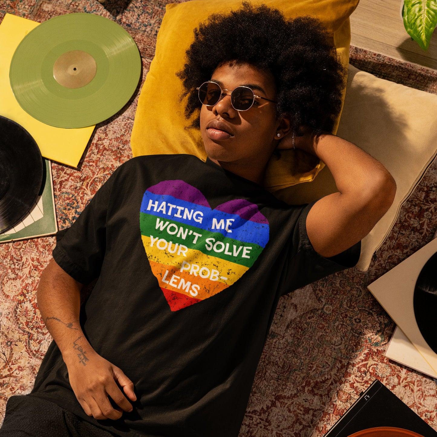 Young person in a No LGBTQ Hate T-shirt with a rainbow-striped heart slogan, surrounded by vinyl records and a potted plant, embodying pride and resistance through bold, unapologetic style.