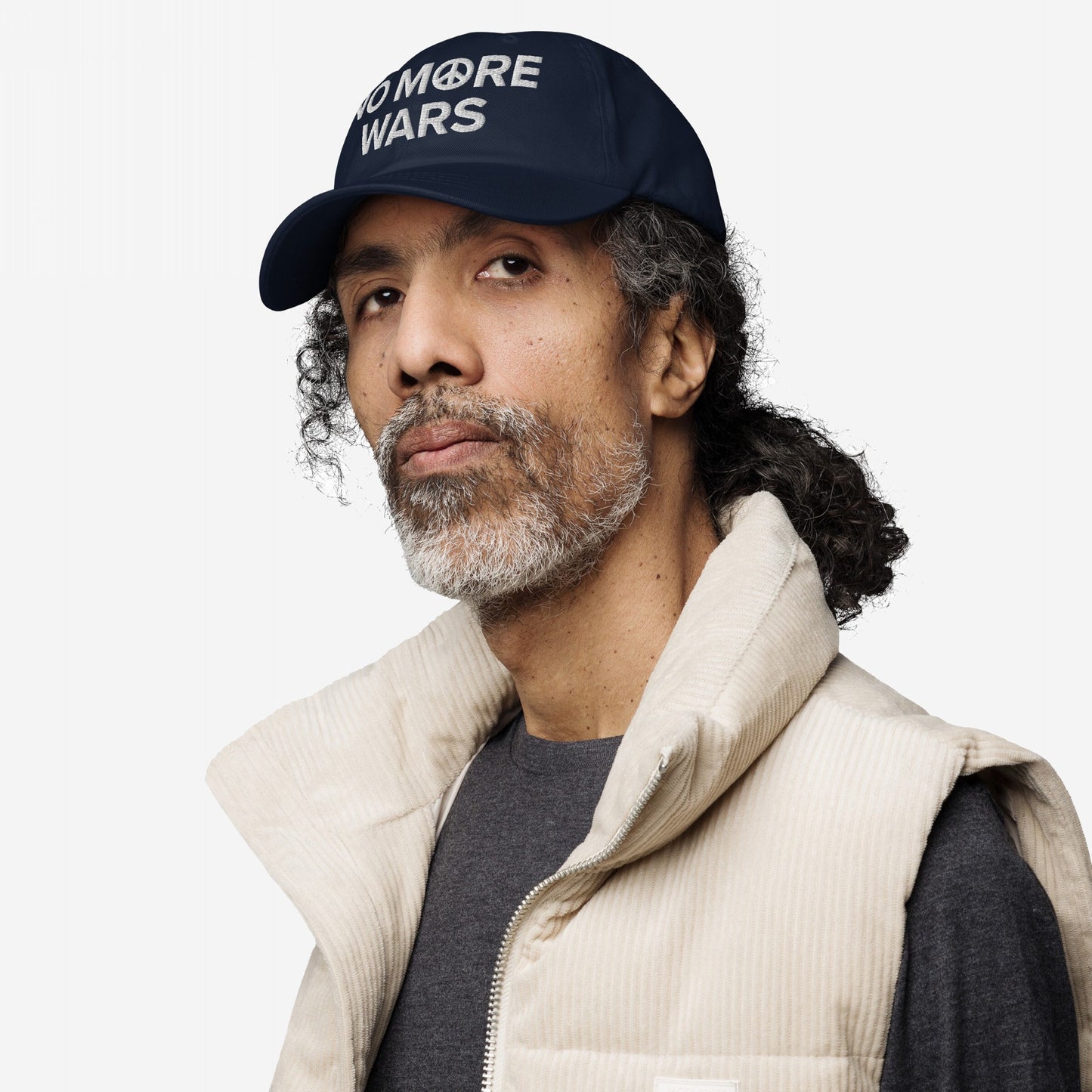 Man wearing the No More Wars Hat, featuring a peace symbol and anti-war slogan. He pairs it with a quilted vest, embodying a bold, protest-ready look.