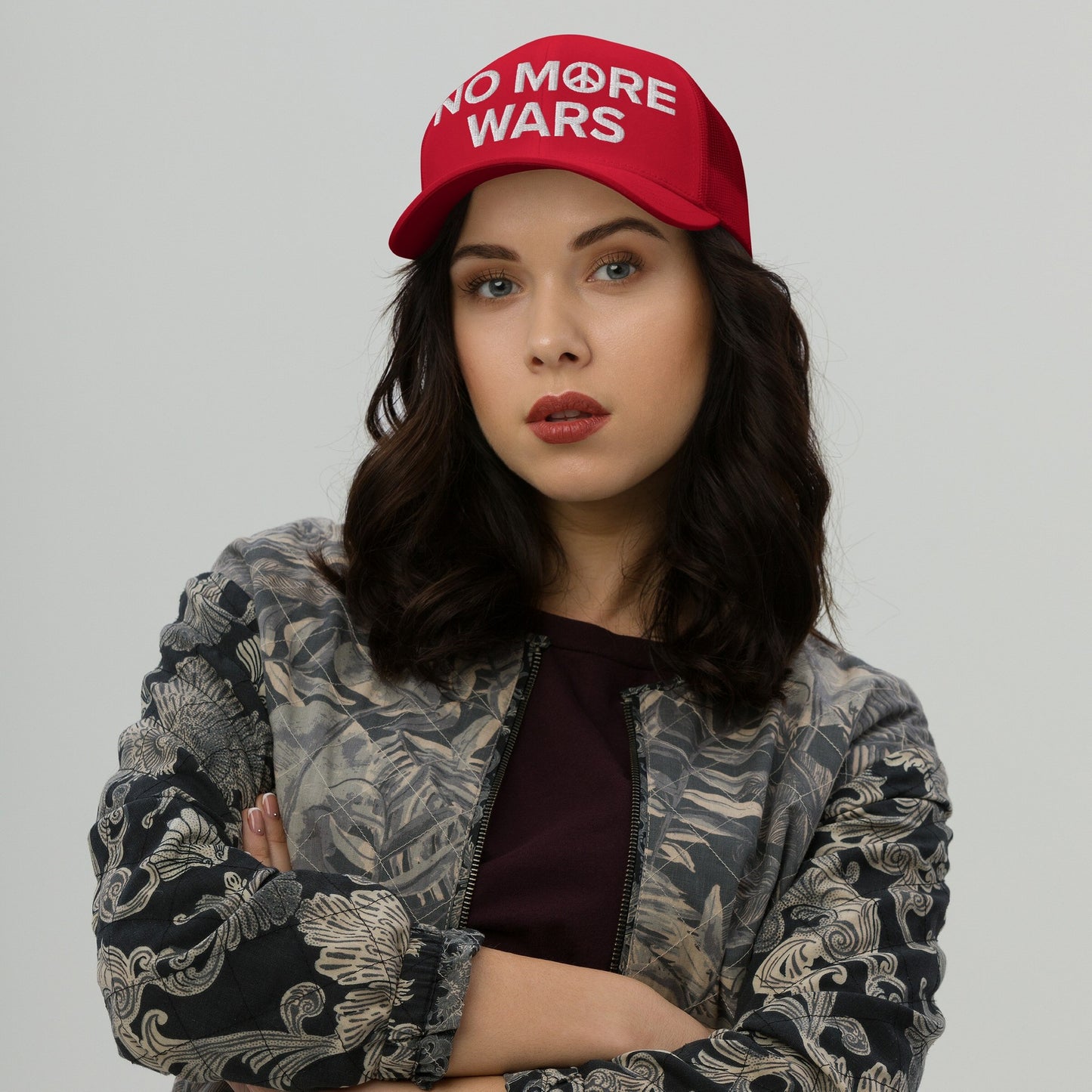 Young woman wearing a No More Wars embroidered cap with a peace symbol, crossing arms, styled in a bomber jacket. This hat boldly conveys an anti-war message, aligning with advocacy for peace and equality.