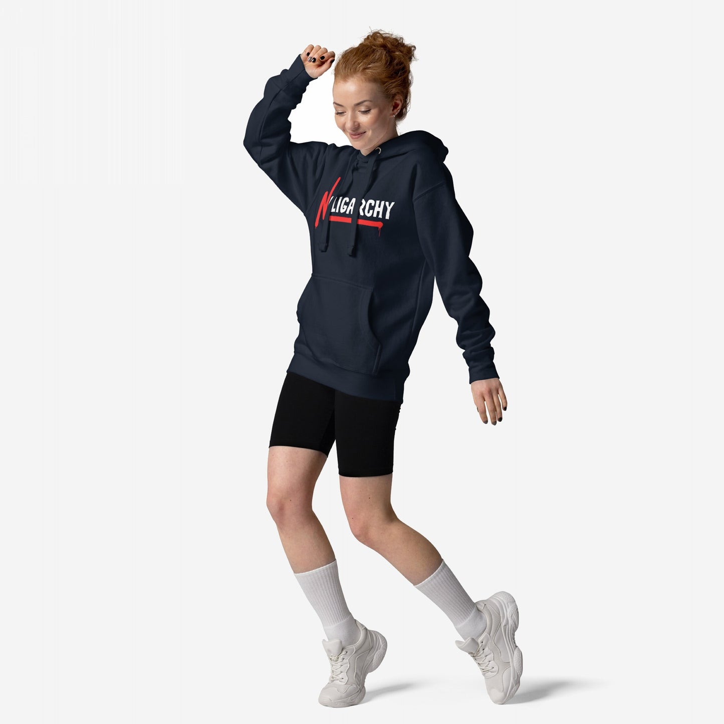 Young woman poses in a No Oligarchy Hoodie, featuring a bold logo with a red slash. She pairs it with black bike shorts and white sneakers, embodying streetwear that sparks conversation.