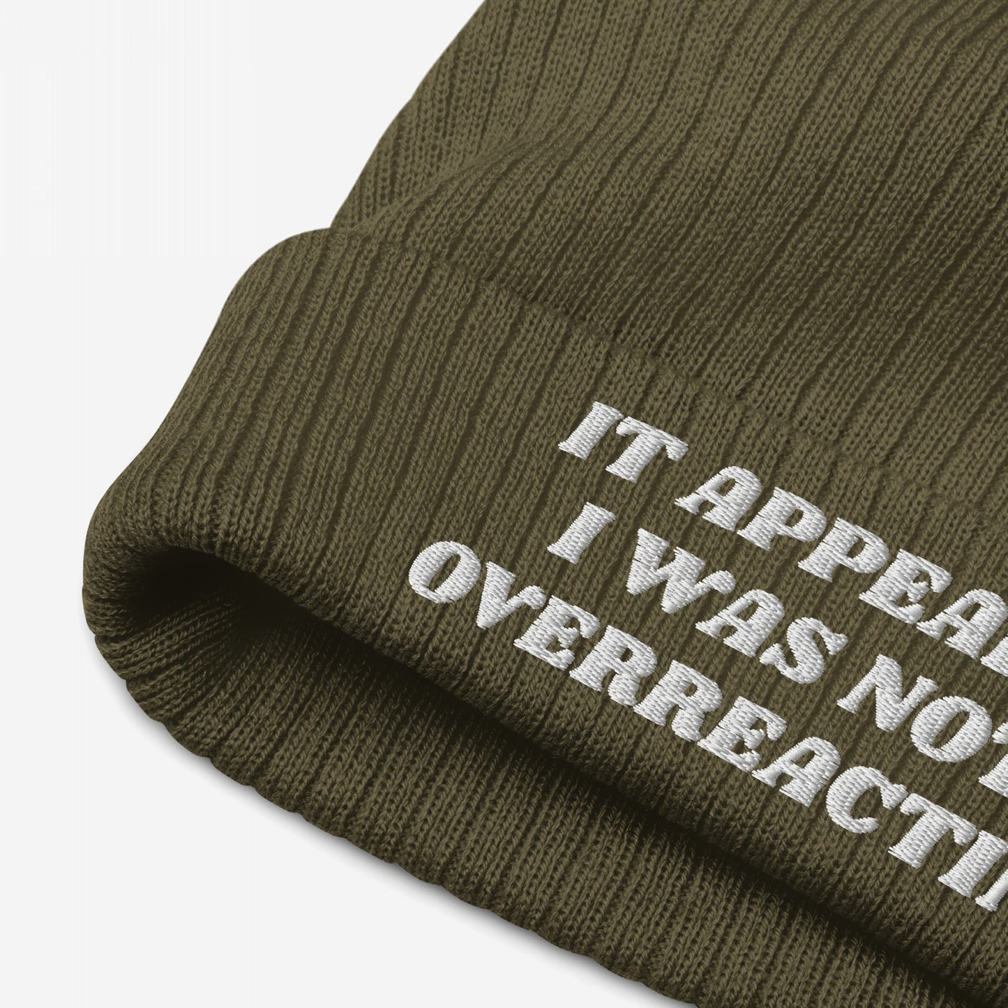 Close-up of the olive-green No More Wars Hat, a ribbed knit beanie featuring a folded cuff with embroidered text It appears I was not overreacting, highlighting an anti-war message.