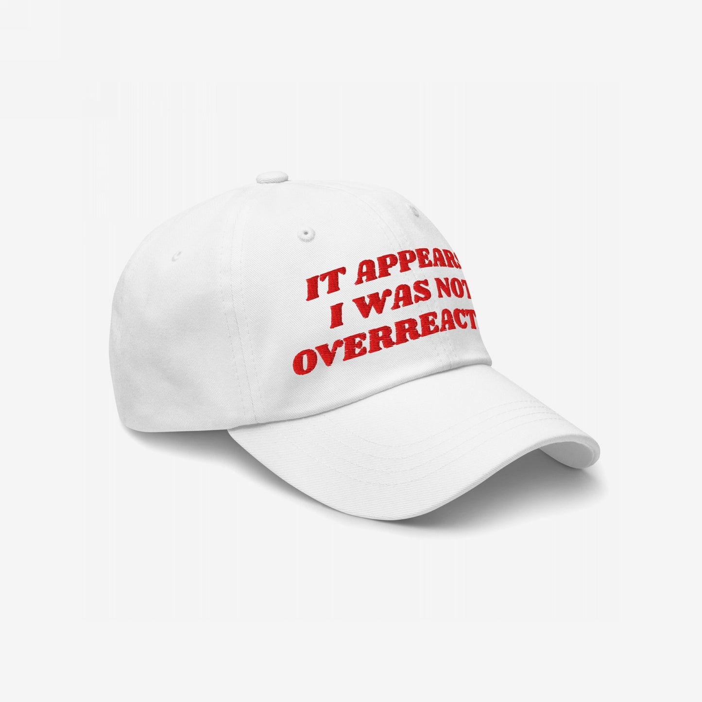 White baseball cap with IT APPEARED I WAS NOT OVERREACTING. embroidered in bold red. The Overreacting Hat symbolizes activism and resistance against political gaslighting, aligning with progressive values and supporting Amnesty International.
