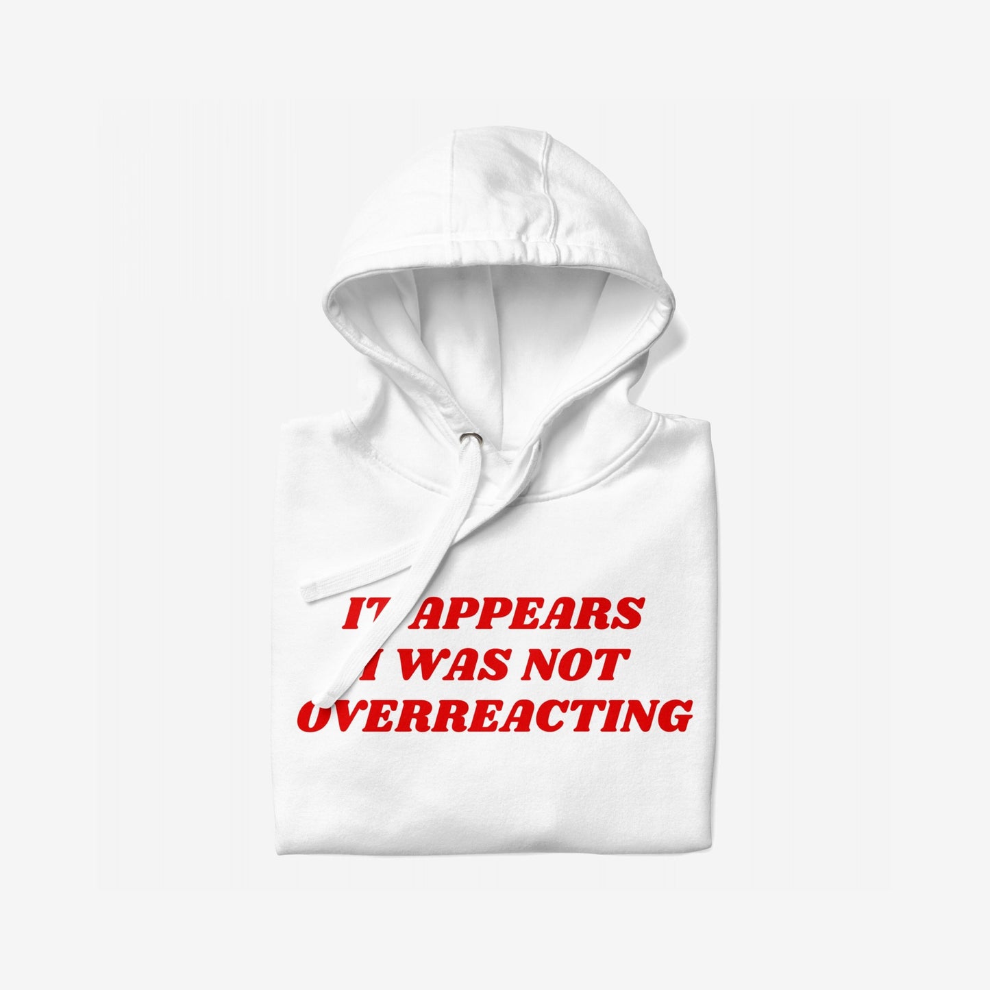 Overreacting Hoodie & Sweatshirt featuring a bold red slogan, “It appears I was not overreacting,” centered on a folded white pullover with visible hood and drawstring, embodying resistance and unapologetic critique.