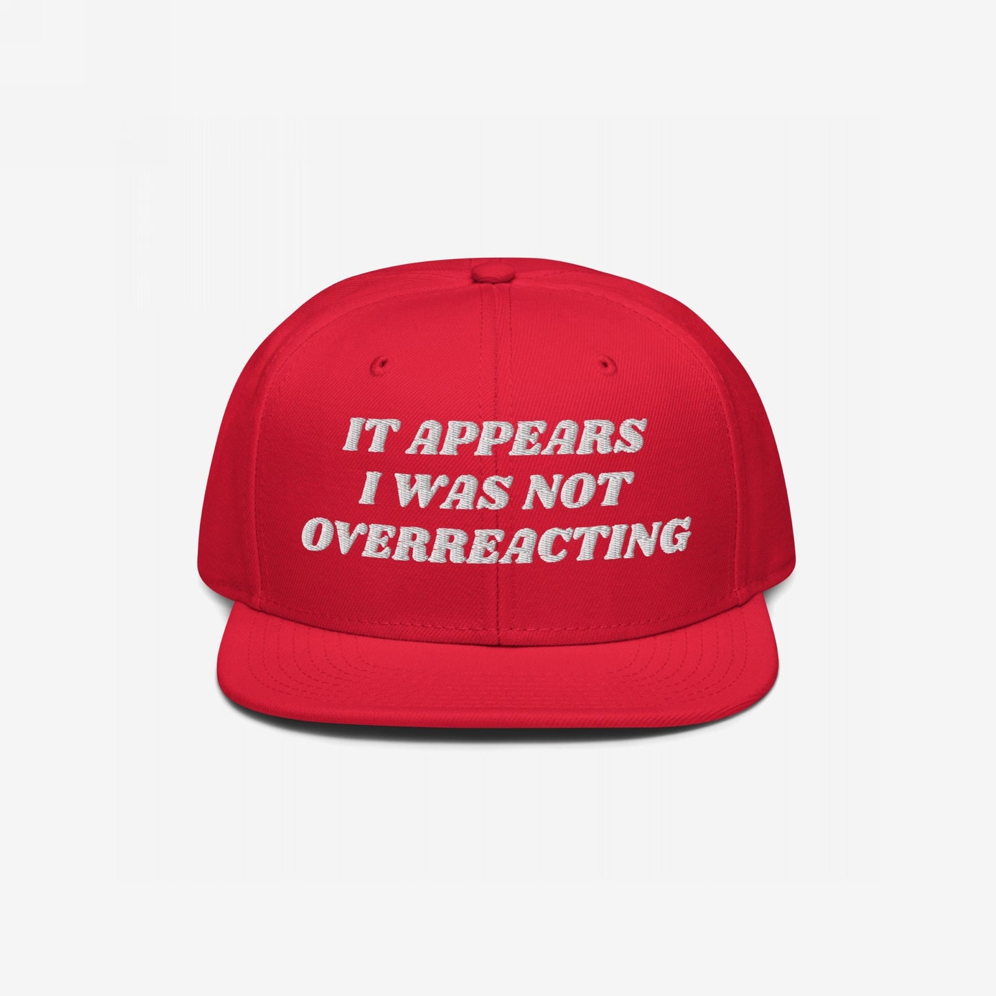The Overreacting Hat features bold white embroidery reading “IT APPEARS I WAS NOT OVERREACTING” on a flat-brim cap, symbolizing resilience against political gaslighting and supporting activist causes.