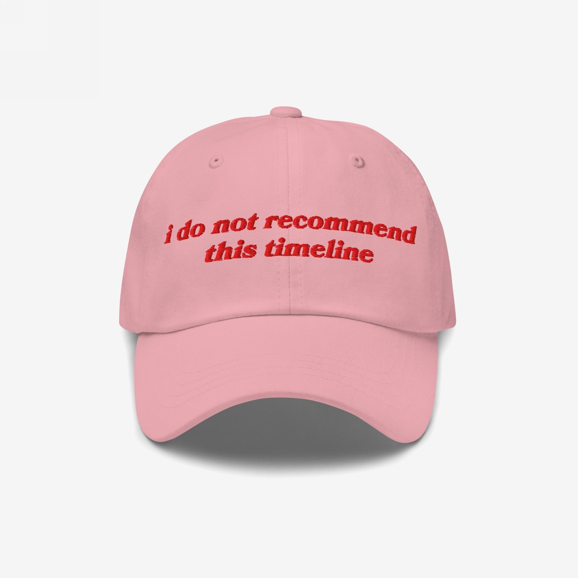 Light pink Timeline Hat with red embroidery stating, “i do not recommend this timeline,” reflecting political humor and irony; perfect for protest gear and supporting mental health causes.