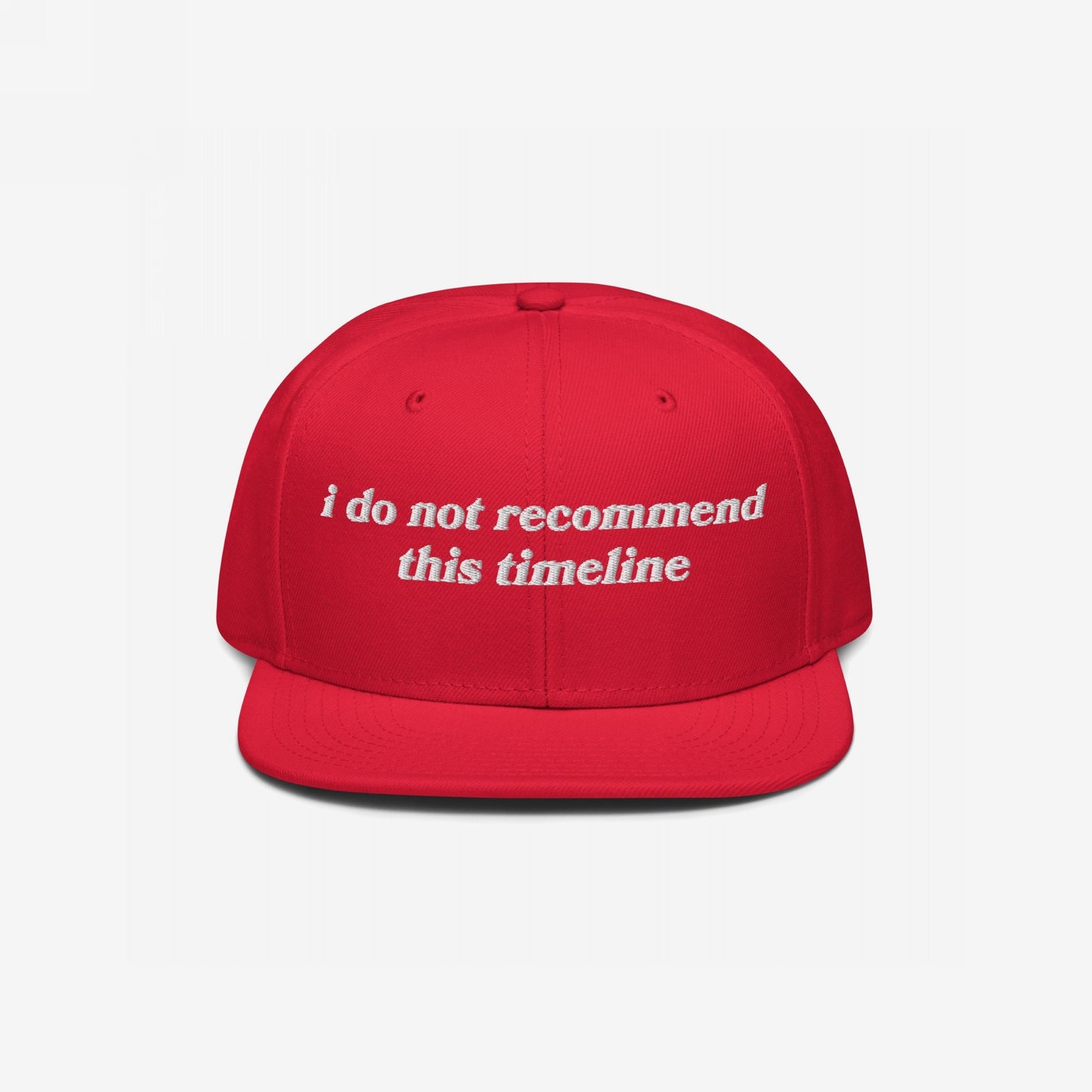 Red flat-bill snapback cap with white embroidered text: “I Do Not Recommend This Timeline.” This Timeline Hat conveys political sarcasm, perfect for expressing discontent with style.