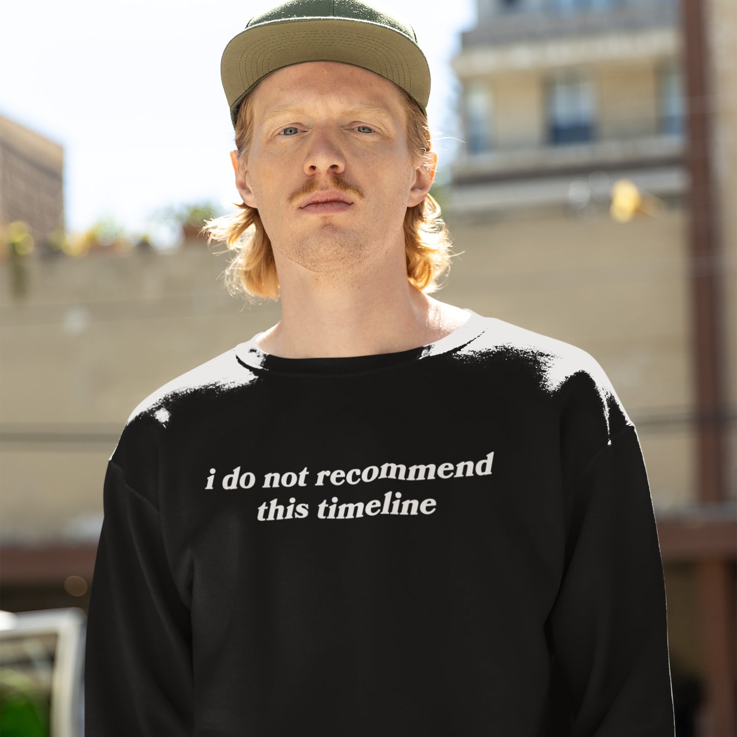 A young man models the Timeline Shirt, a black sweatshirt with bold white text critiquing modern times, embodying a blend of humor and social commentary.