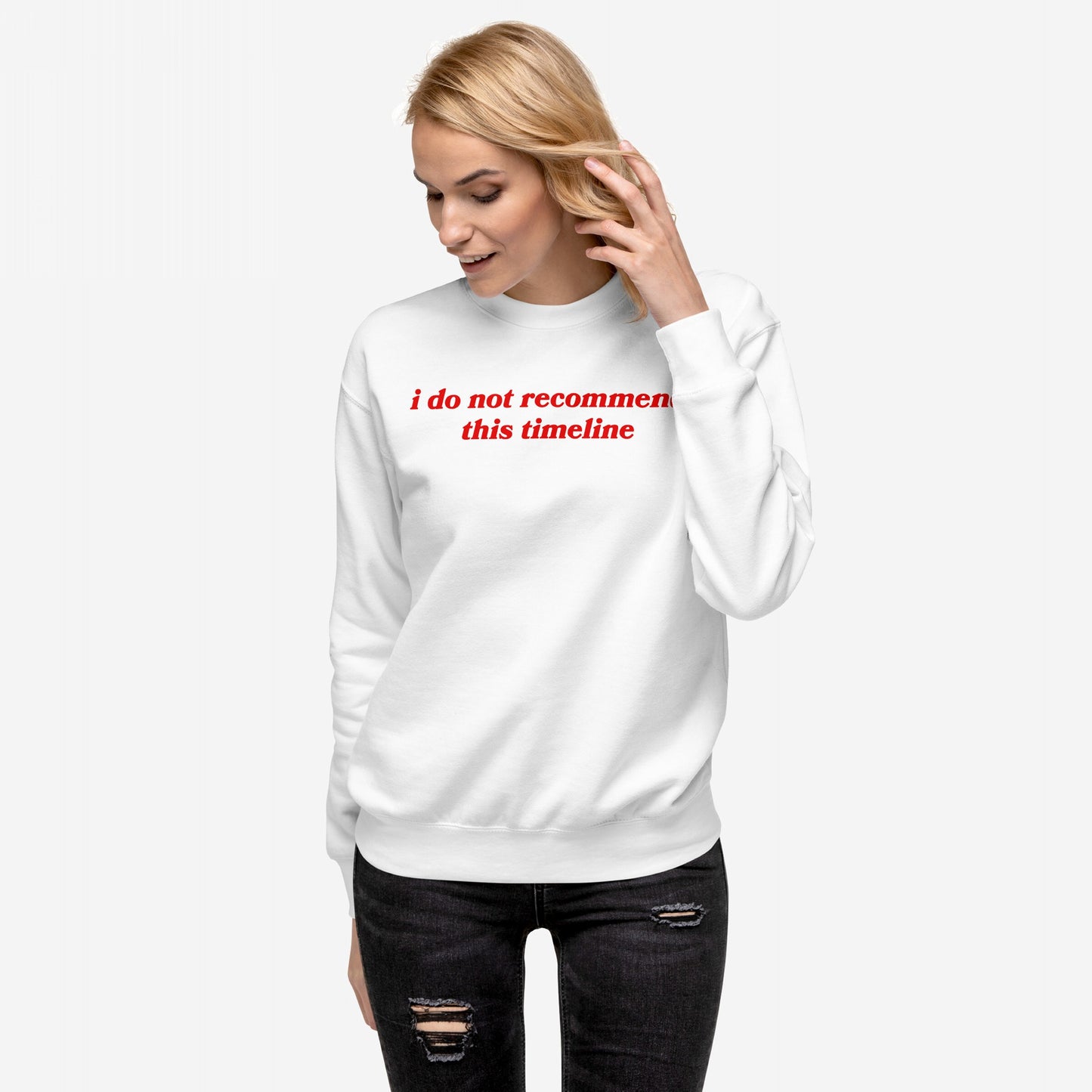 Blonde woman in a Timeline Hoodie & Sweatshirt, featuring bold red text, i do not recommend this timeline, paired with black distressed jeans, embodying sarcasm and dystopian style.