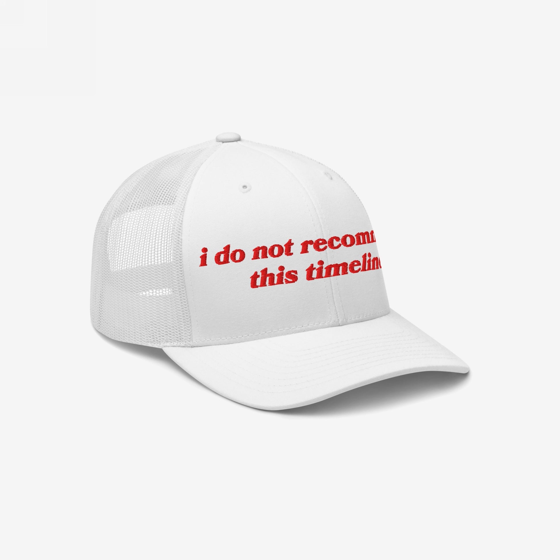White mesh-back trucker cap with a curved bill, featuring bold red embroidery stating i do not recommend this timeline. The Timeline Hat humorously reflects today's chaotic world.