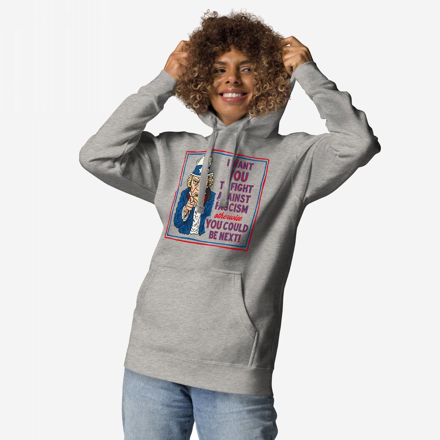 Person in a light-gray Anti-Fascist Uncle Sam Hoodie, featuring a bold graphic urging resistance to fascism. They're smiling, lifting the hood, embodying the message of activism and defiance.