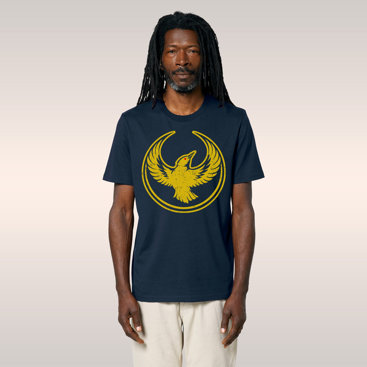 Man wearing an Oregon Rebel Alliance T-shirt featuring a yellow stylized bird emblem, standing outdoors with greenery and a f