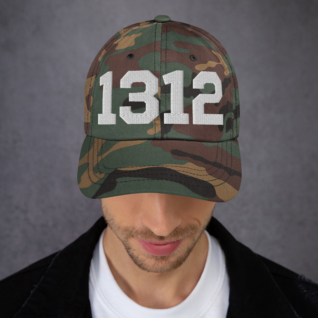 Person wearing a woodland-pattern camouflage baseball cap with bold white 1312 on the front, representing the protest code ACAB. Ideal for those advocating police accountability and standing against brutality.