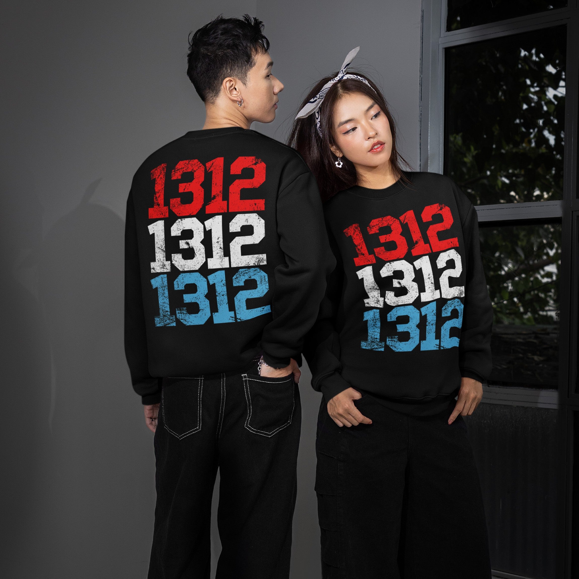 1312 ACAB Sweatshirt features stacked distressed numbers in red, white, blue. Female model shows front; male shows back. Represents anti-police brutality stance. Ideal for protests or everyday advocacy.