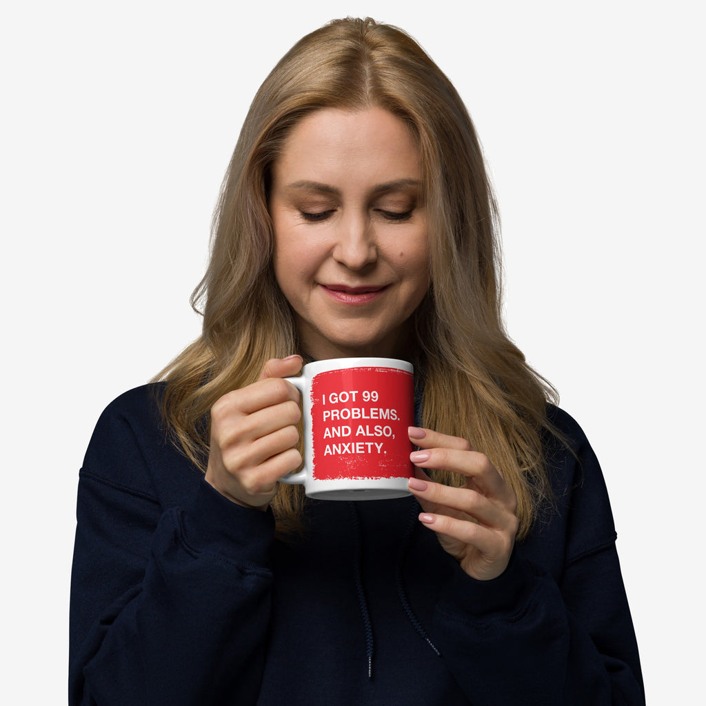 Woman holding 99 Problems Mug with bold text I GOT 99 PROBLEMS. AND ALSO, ANXIETY. on a white background; embodying a blend of humor and solidarity, ideal for stress-filled mornings.