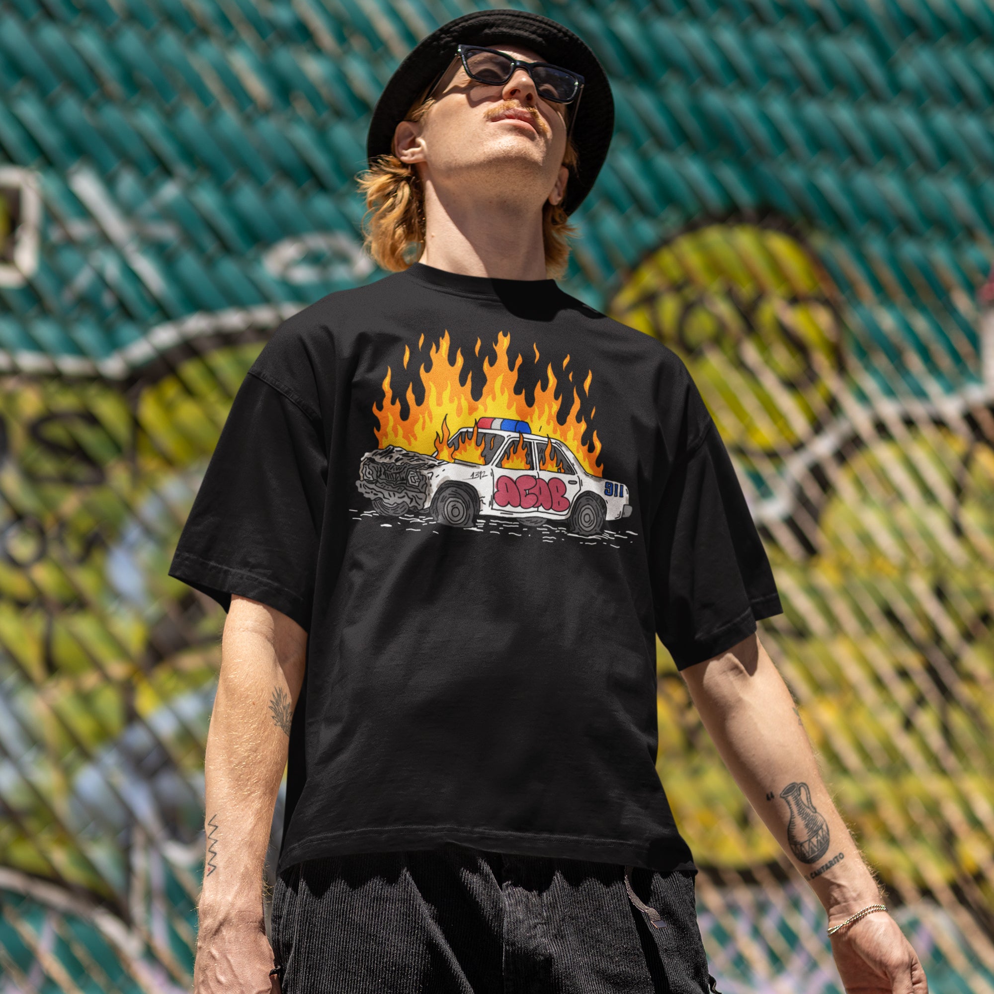 Man wearing ACAB Police Car Shirt with hand-drawn flaming police car and graffiti 1312 design in urban setting
