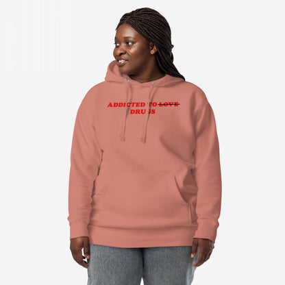 Person in a muted rose-pink Addicted To Love / Drugs Hoodie & Sweatshirt, featuring bold red text with Love crossed out, paired with light-wash jeans, embodying raw, reflective streetwear.