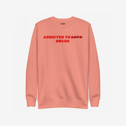 Muted coral crew-neck sweatshirt with bold red text: Addicted to ̶L̶O̶V̶E̶ DRUGS. LOVE is crossed out, symbolizing a raw, honest twist on classic themes.