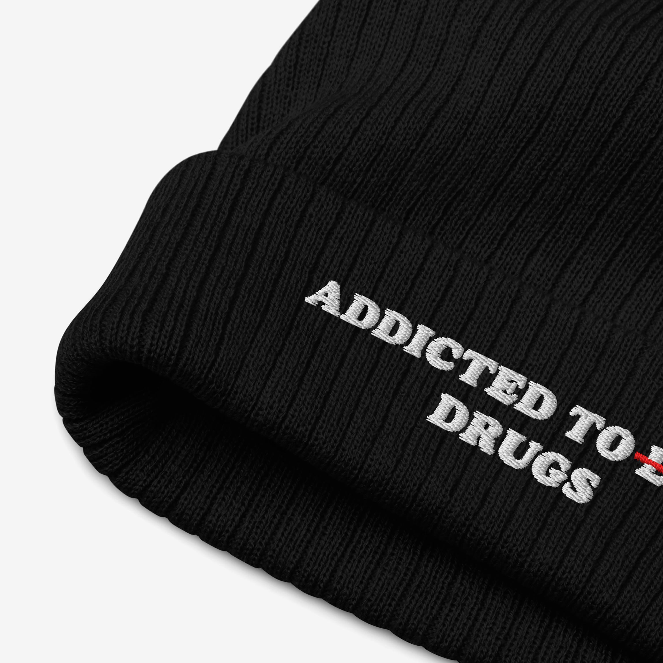 Close-up of black knit beanie featuring embroidered text "Addicted To Love" with "Love" crossed out and replaced by "Drugs" on Addicted To Love / Drugs Hat.