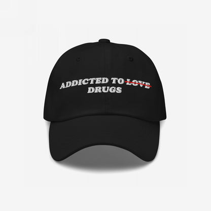 Black cap with bold white embroidery, ADDICTED TO LOVE, with LOVE crossed out in red, revealing DRUGS. A statement piece reflecting raw honesty and challenging societal norms.