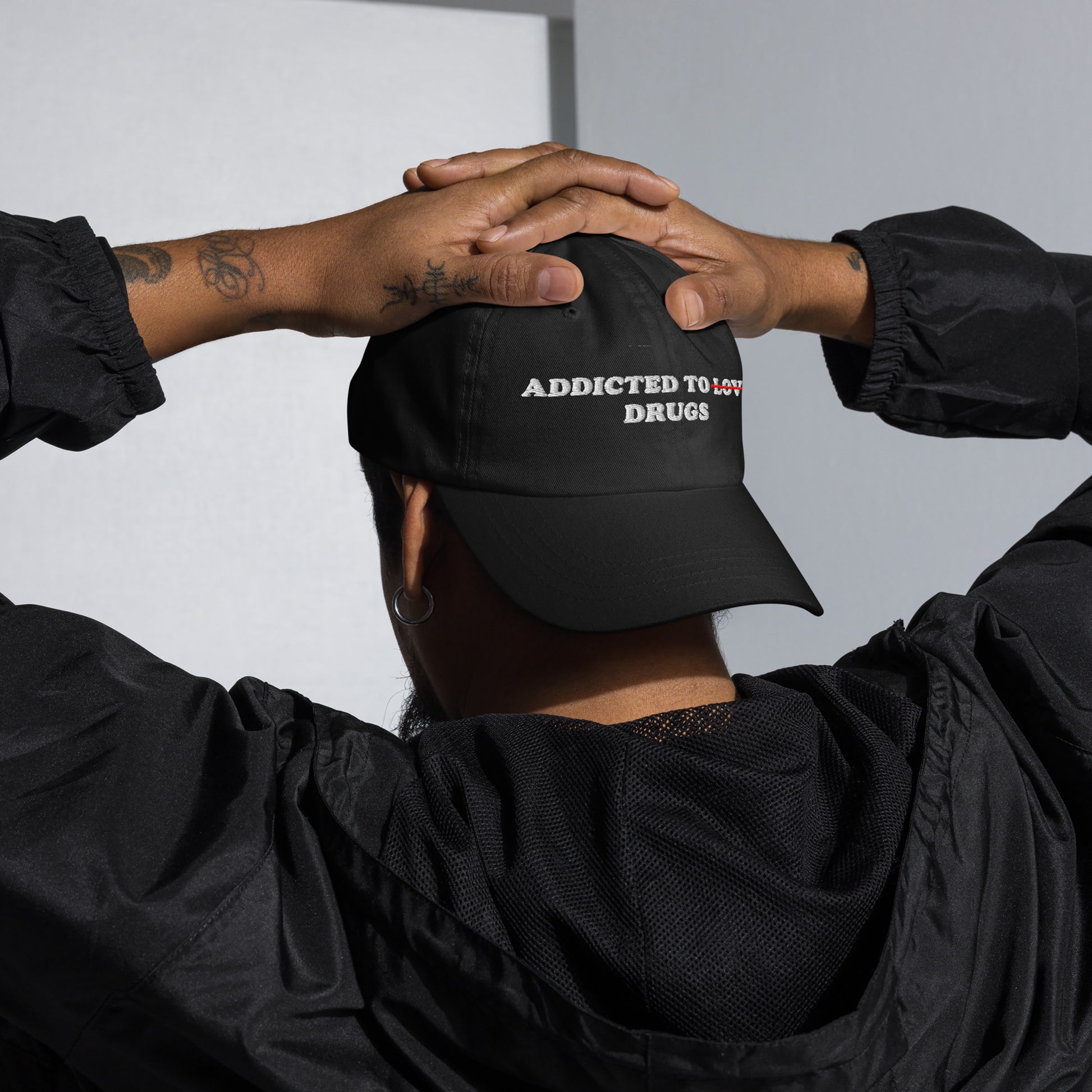 Person wearing black Addicted To Love / Drugs Hat with "Love" crossed out and replaced by "Drugs" embroidered on front panel.