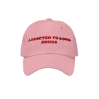 Pink embroidered "Addicted To Love / Drugs Hat" with "Love" crossed out and replaced by "Drugs" in bold red text on front.