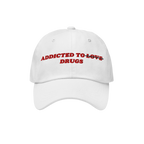 White snapback hat with "Addicted To Love" crossed out and replaced by "Drugs" embroidered in red, titled Addicted To Love / 