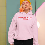 Woman wearing pink hoodie with "Addicted To Love / Drugs Shirt" bold design text crossed out love replaced by drugs.