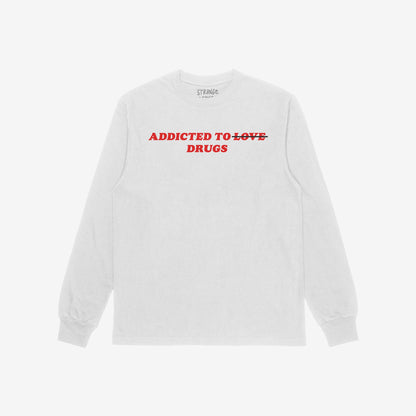 Light-gray long-sleeve T-shirt with bold red text: ADDICTED TO ~LOVE~ DRUGS. LOVE is crossed out. The Addicted To Love / Drugs T-shirt blends irony and edge, reflecting bold honesty.