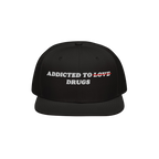 Black snapback hat with embroidered text "Addicted To Love" crossed out and replaced by "Drugs" on the Addicted To Love / Dru