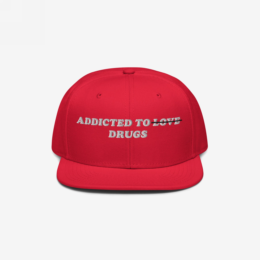 Red snapback hat with embroidered "Addicted To Love" crossed out and replaced by "Drugs" text, titled Addicted To Love / Drugs Hat.