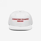 White snapback hat with red embroidered text "Addicted to ~Love~ Drugs" front design, titled Addicted To Love / Drugs Hat.
