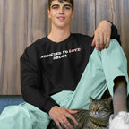 Young man wearing black Addicted To Love / Drugs Shirt with crossed out “Love” replaced by “Drugs,” sitting with cat against wood background