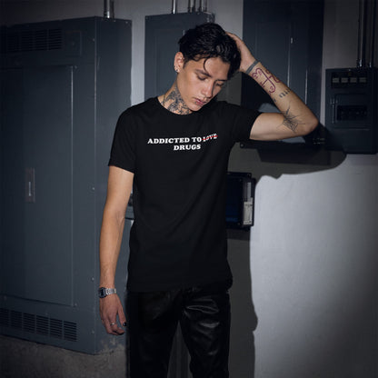A young person in an industrial setting wears the Addicted To Love / Drugs T-shirt, featuring a bold statement with a crossed-out Love and prominent Drugs, reflecting edgy, unapologetic style.