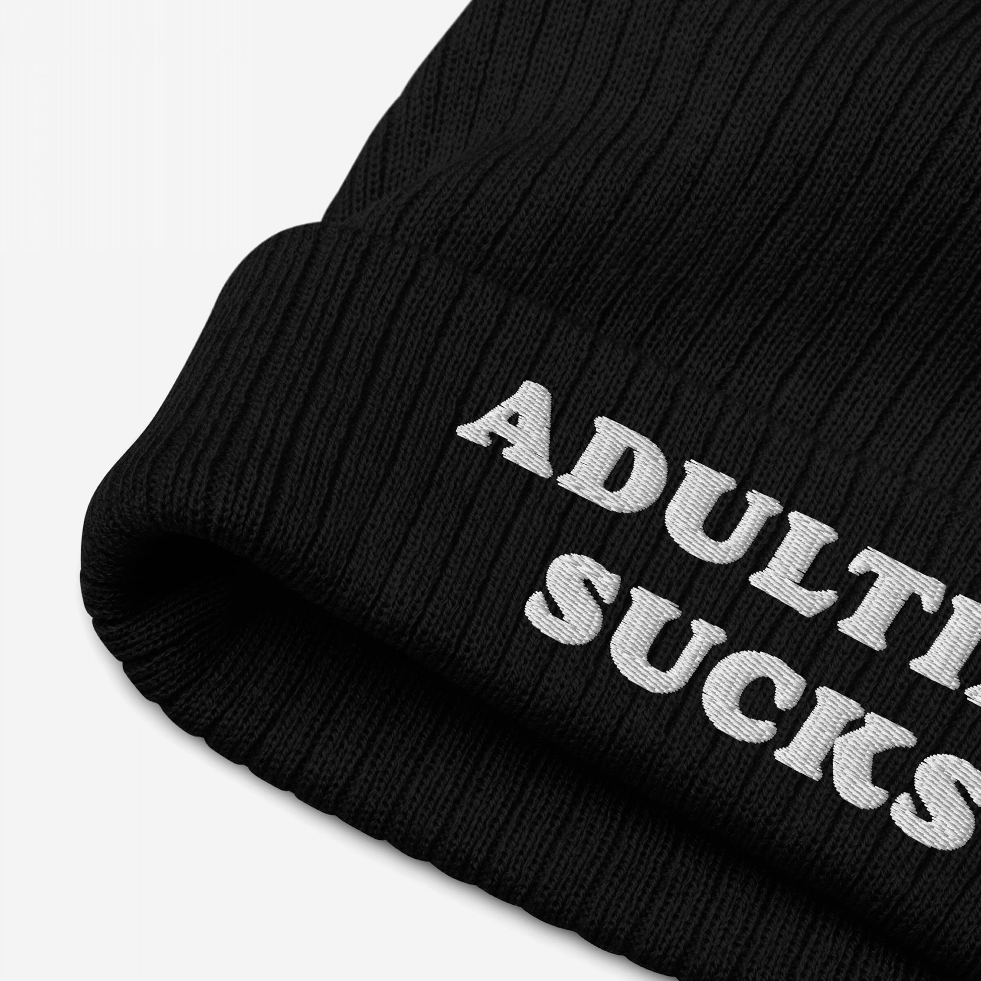 Black rib-knit cuffed beanie with “ADULTING SUCKS” embroidered in white on the brim, embodying a candid message for those navigating life's challenges. Supports Amnesty International.