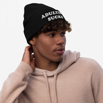Young person wearing an Adulting Sucks knit beanie, capturing the overworked vibe. The hat features bold, white embroidered text, reflecting the product's candid message amidst life's challenges.