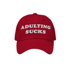 Red baseball cap with ADULTING SUCKS embroidered in bold white letters, capturing a vintage-inspired style perfect for expres