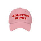 Pink baseball-style cap with bold red embroidery reading ADULTING SUCKS, highlighting a playful, relatable message for those 