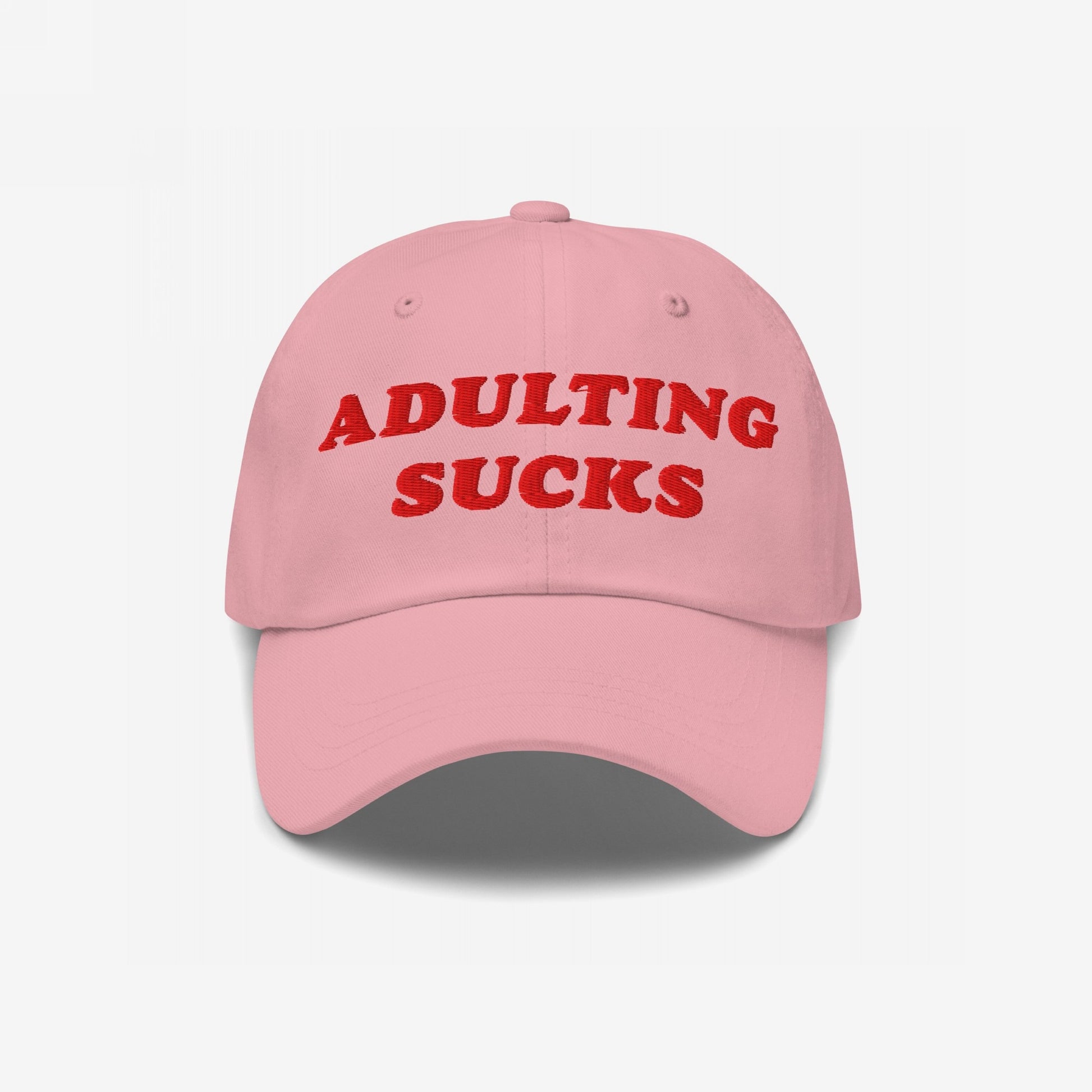 Light pink baseball cap with ADULTING SUCKS in bold red embroidery, expressing a humorous take on life's challenges. The cap embodies a candid and relatable message about adulthood's struggles.