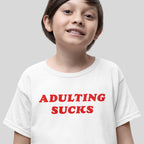 Young boy wearing an Adulting Sucks T-shirt with bold red lettering, humorously capturing the challenges of grown-up life with a casual, expressive design ideal for all ages.