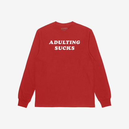 Red long-sleeve T-shirt with ADULTING SUCKS in bold white letters across the chest, featuring a retro typeface. Part of a collection supporting equality and self-expression.