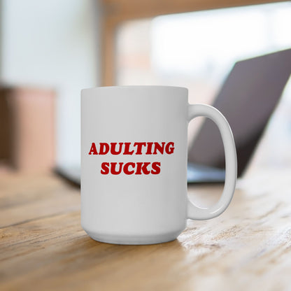 A white ceramic mug with ADULTING SUCKS in bold red letters, perfect for expressing morning frustrations. Ideal for anyone navigating modern adulthood, this mug offers humor and resilience in every sip.