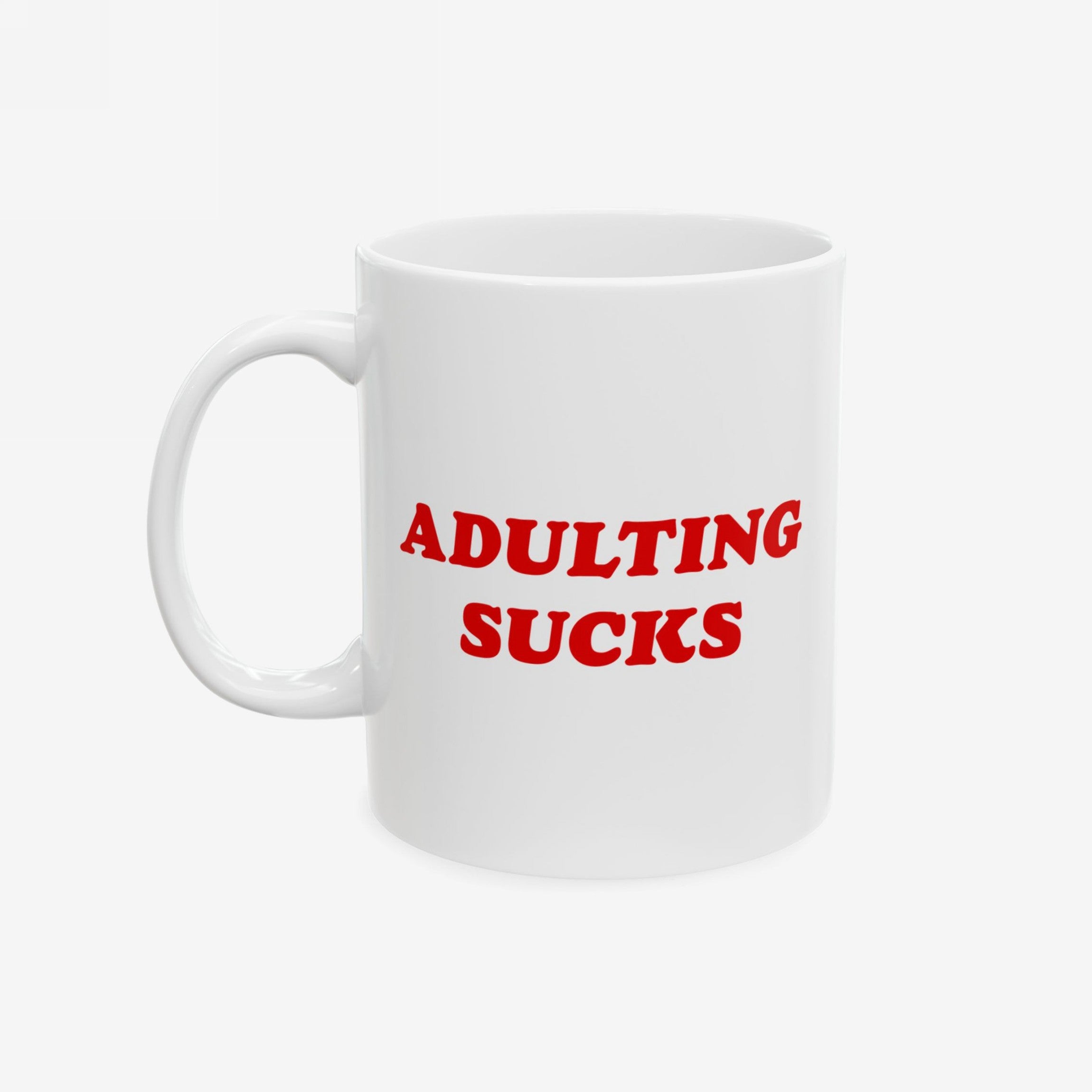 White ceramic mug with bold red “Adulting Sucks” text, shown with the handle on the left side against a plain backdrop