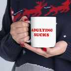 Close-up of hands holding “Adulting Sucks” mug, red nails and cozy winter sweater in frame, sipping through seasonal burnout