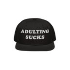 Black snapback hat with white, bold embroidered text ADULTING SUCKS on the front. Perfect for expressing frustration with adu
